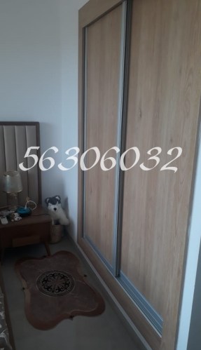 Image of a wooden wardrobe with sliding doors in a modern bedroom, featuring a bedside table with a lamp and a decorative rug on the floor.